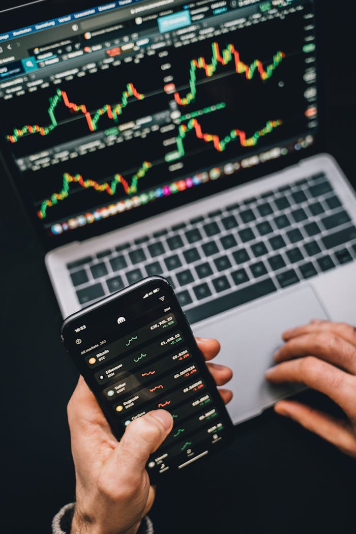 about-04 Person analyzing stock market data with a laptop and smartphone showing trading graphs.
