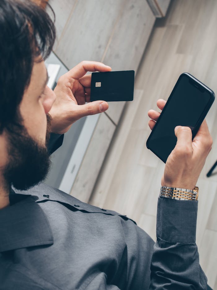 about-03 Adult man using a smartphone for online transactions while holding a credit card indoors.